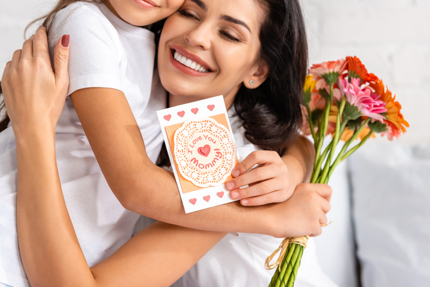 boldog nő ölelés lánya kezében virágok és anyák napi kártya veled szeretlek anyu felirat - Fotó, kép