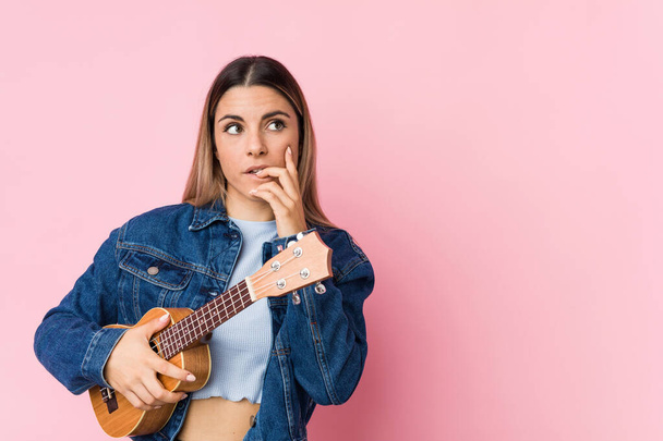 Young caucasian woman playing ukelele relaxed thinking about something looking at a copy space. - Photo, Image