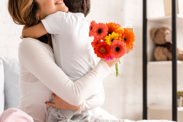 rajattu näkymä onnellinen äiti halaus poika pitäen kukkia äitien päivä
 - Valokuva, kuva