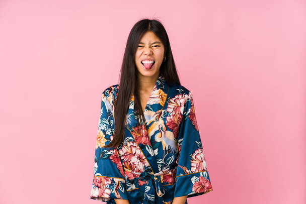 Joven asiático mujer usando un kimono pijama divertido y amigable sobresaliendo lengua
. - Foto, Imagen