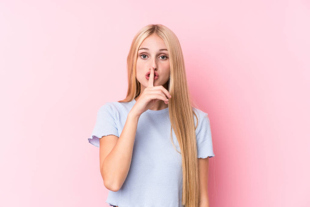 Young blonde woman on pink background keeping a secret or asking for silence. - Photo, Image