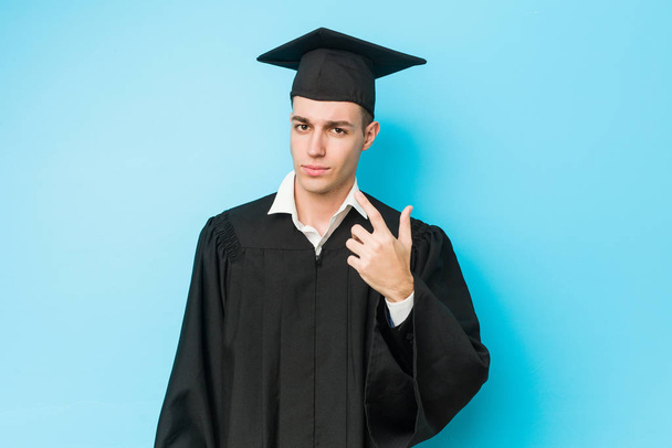 Молодой кавказский выпускник показывает пальцем на тебя, как будто приглашая подойти ближе.
. - Фото, изображение