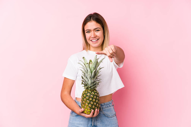 Jeune femme caucasienne tenant un sourire joyeux ananas pointant vers l'avant
. - Photo, image