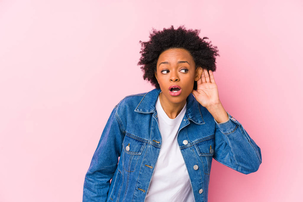 Молодая африканская американка против розового фона, изолированная, пытающаяся слушать сплетни
. - Фото, изображение