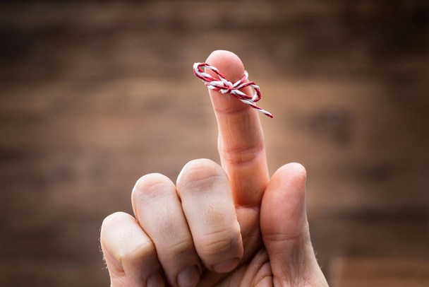Close-up Of Person's Finger With Tied Ribbon Bow Over Gray Background - Фото, изображение