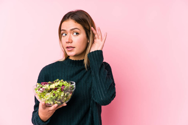 Jonge blanke vrouw houdt een salade geïsoleerd proberen om een roddel te luisteren. - Foto, afbeelding