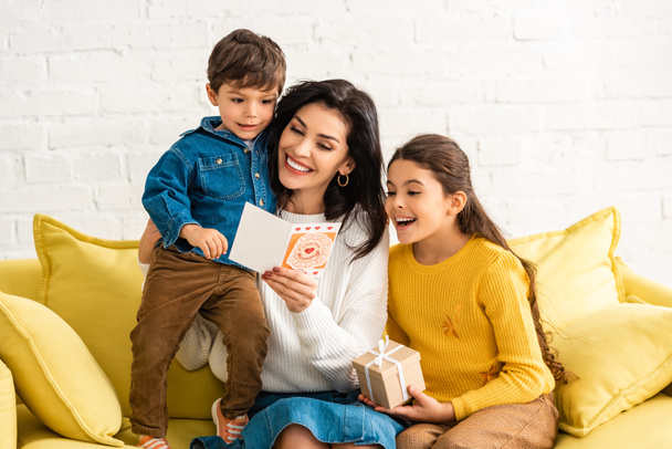 boldog nő kezében anyák napi kártya és átölelő fia, míg a lánya kezében ajándék doboz - Fotó, kép