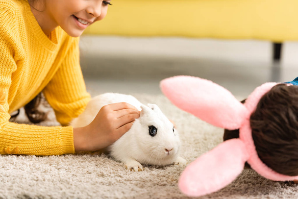 bijgesneden weergave van kinderen liggend op de vloer in de buurt van wit grappig konijn - Foto, afbeelding