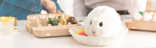 Paskalya yumurtaları ve beyaz tavşanlı panoramik resimli masanın yanındaki kadın ve çocuk manzarası. - Fotoğraf, Görsel