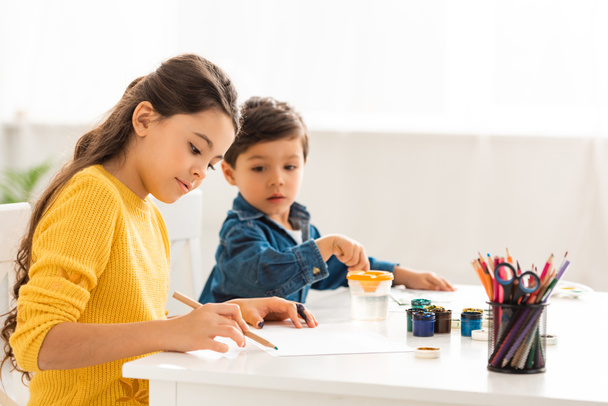 selective focus of cute boy looking at sister drawing with pencil - Photo, Image
