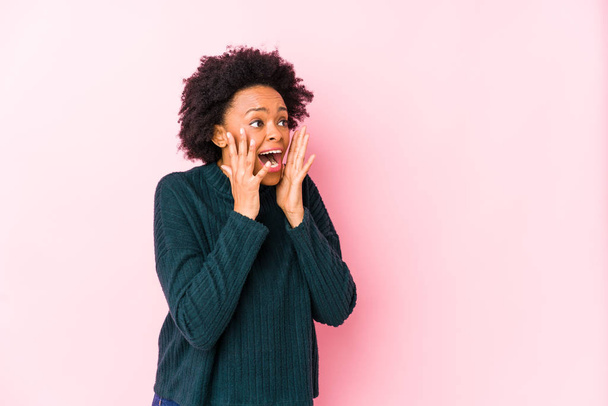 Középkorú afro-amerikai nő ellen rózsaszín háttér elszigetelt kiabál hangosan, tartja nyitva a szemét, és a kezét feszült. - Fotó, kép