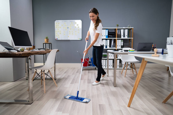 Full Length Of Female Janitor Mopping Floor In Office - Foto, afbeelding