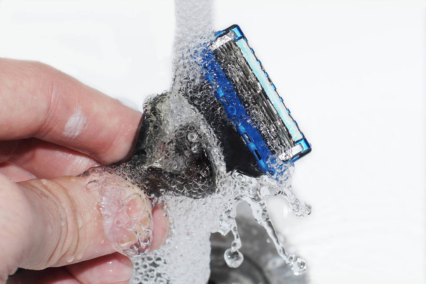 Scheermes in je hand wordt gewassen onder een stroom schoon water. Gezichtsverzorging en hygiëne. Gezondheidszorg. - Foto, afbeelding