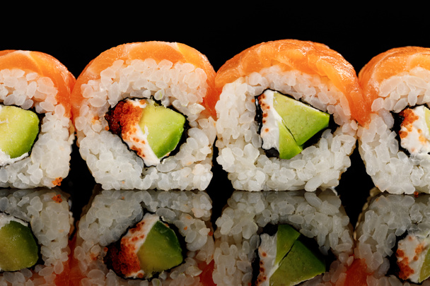 φρέσκο νόστιμο sushi Φιλαδέλφεια με αβοκάντο, κρεμώδες τυρί, σολομό και χαβιάρι masago απομονώνονται σε μαύρο χρώμα με αντανάκλαση - Φωτογραφία, εικόνα