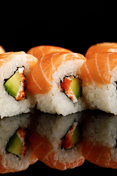 close up view of fresh delicious Philadelphia sushi with avocado, creamy cheese, salmon and masago caviar isolated on black with reflection - Foto, Bild