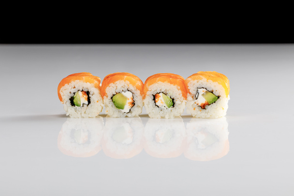 delicious Philadelphia sushi with avocado, creamy cheese, salmon and masago caviar on white surface isolated on black - Photo, Image