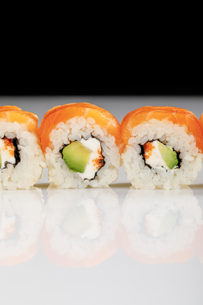 close up view of delicious Philadelphia sushi with avocado, creamy cheese, salmon and masago caviar on white surface isolated on black - Photo, Image