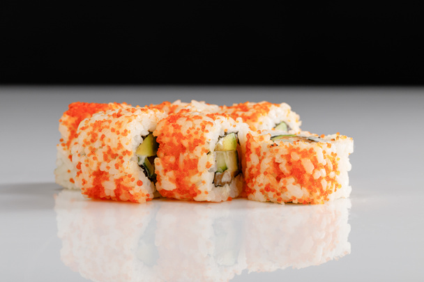 delicious California roll with avocado, salmon and masago caviar on white surface isolated on black - Фото, изображение