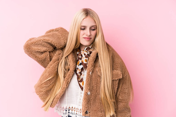 Молода блондинка в пальто на рожевому фоні страждає від болю в шиї через сидячий спосіб життя
. - Фото, зображення