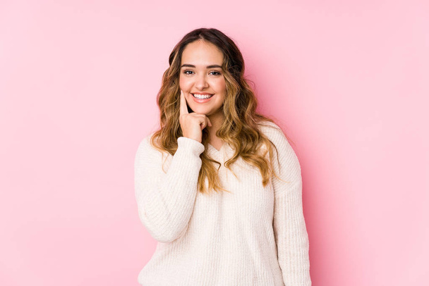 Young curvy woman posing in a pink background isolated smiling happy and confident, touching chin with hand. - Photo, Image