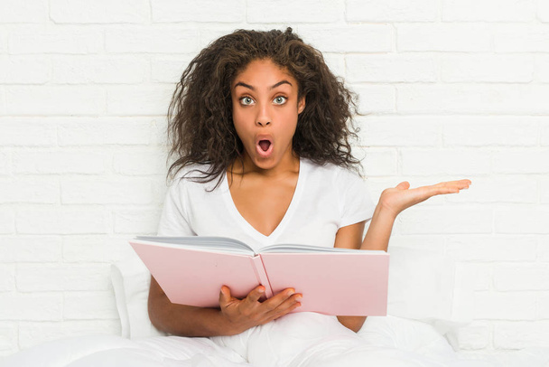 Mladá africká americká žena sedí na posteli a studuje ohromen držení kopie prostoru na dlani. - Fotografie, Obrázek