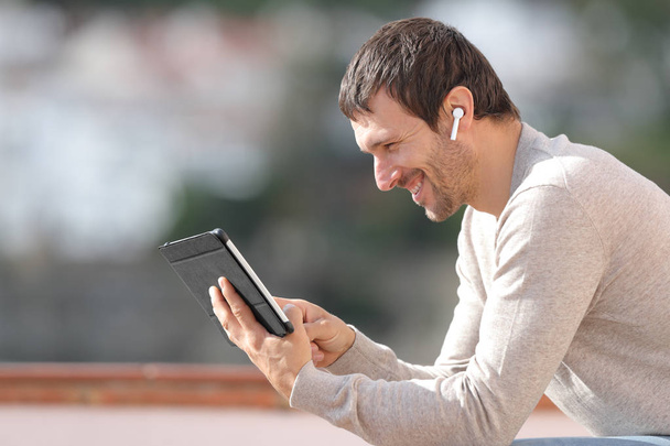 Profile of happy man watching media with tablet and earbuds - Foto, Bild