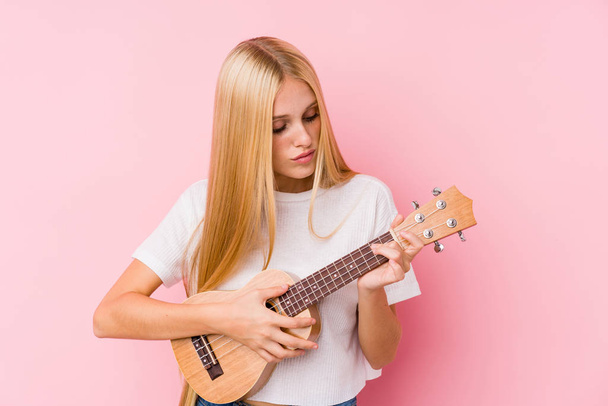 Young blonde woman playing ukelele isolated in a background - Foto, imagen