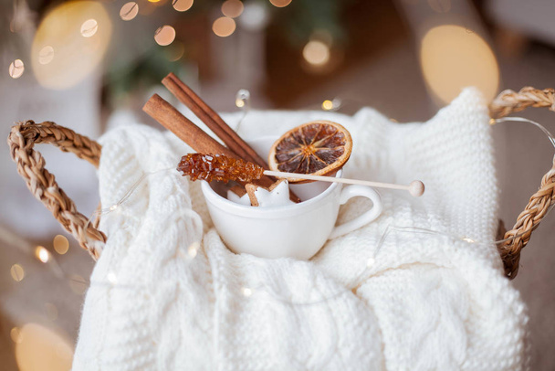 Ψάθινο καλάθι, πλεκτό πουλόβερ, ξερά κίτρα, ξυλάκια κανέλας, χριστουγεννιάτικα μπισκότα, χριστουγεννιάτικα φώτα. Άνετο.. - Φωτογραφία, εικόνα