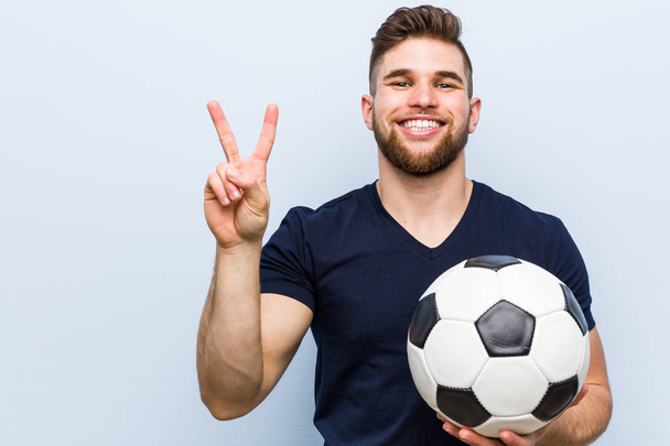Молодий білий чоловік тримає футбольний м'яч, показуючи номер два пальцями
. - Фото, зображення