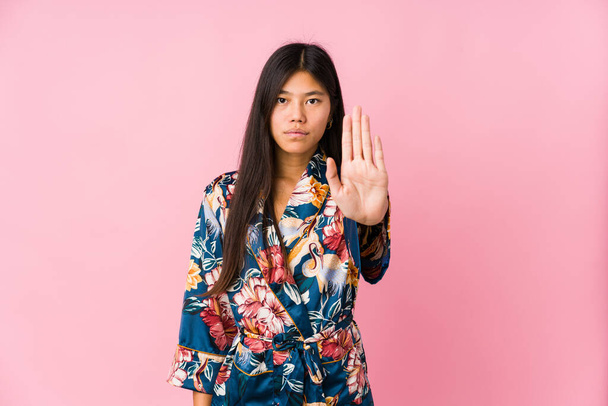 Joven mujer asiática usando un pijama kimono de pie con la mano extendida mostrando señal de stop, previniéndote
. - Foto, imagen