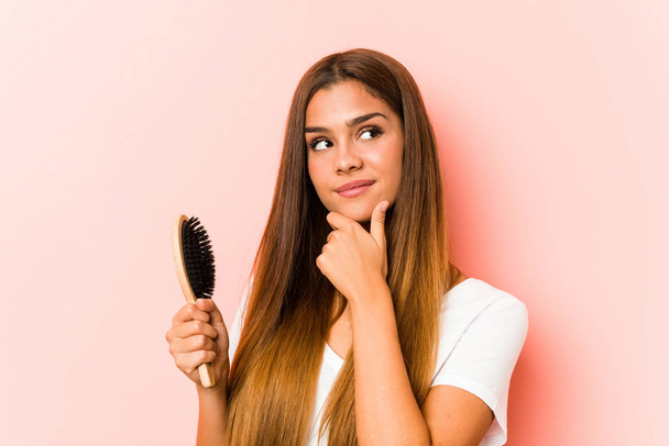 Young caucasian woman holding an hairbrush looking sideways with doubtful and skeptical expression. - Zdjęcie, obraz