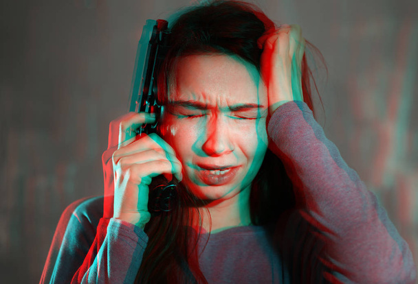 junge depressive Frau mit Waffe denkt vor grauem Hintergrund über Selbstmord nach - Foto, Bild