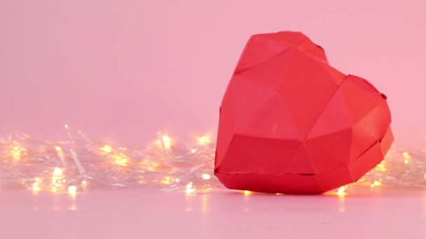Χαρτί γεωμετρικό 3d σχήμα καρδιάς με χρυσά φώτα γιρλάντα σε ροζ φόντο. - Πλάνα, βίντεο