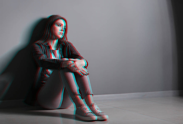 Mujer joven deprimida sentada cerca de la pared gris
 - Foto, Imagen