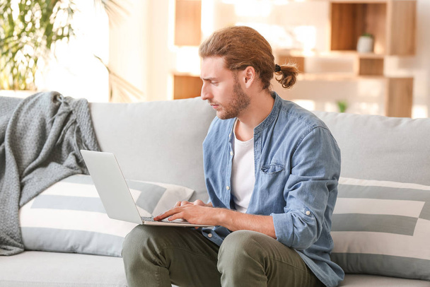 Handsome man with laptop on sofa at home - Photo, image