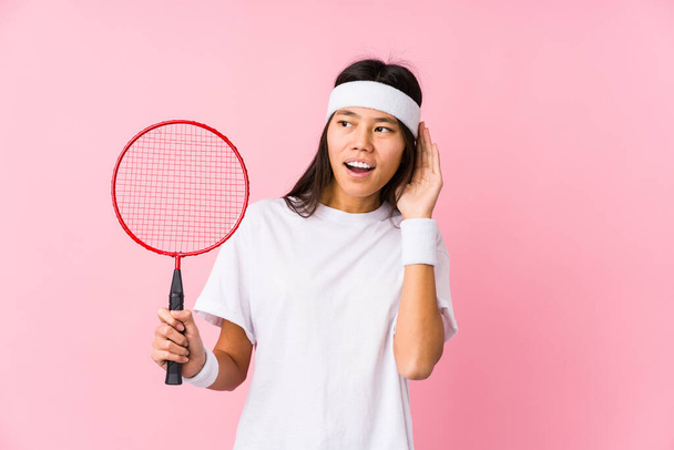 Młoda Chinka grająca badmintona w różowym tle, próbująca słuchać plotek. - Zdjęcie, obraz