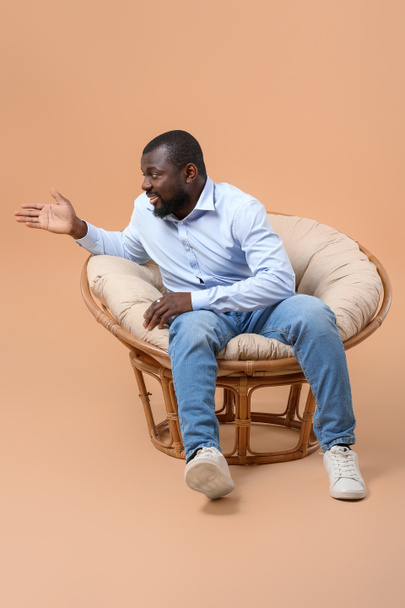 Αφροαμερικανός που κάθεται στην πολυθρόνα με φόντο το χρώμα - Φωτογραφία, εικόνα
