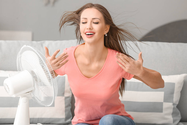 Молода жінка використовує електричний вентилятор під час теплової хвилі вдома
 - Фото, зображення