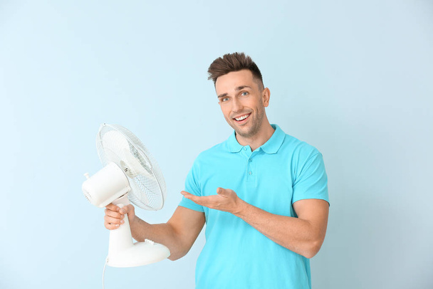 Giovane uomo con ventilatore elettrico su sfondo a colori
 - Foto, immagini