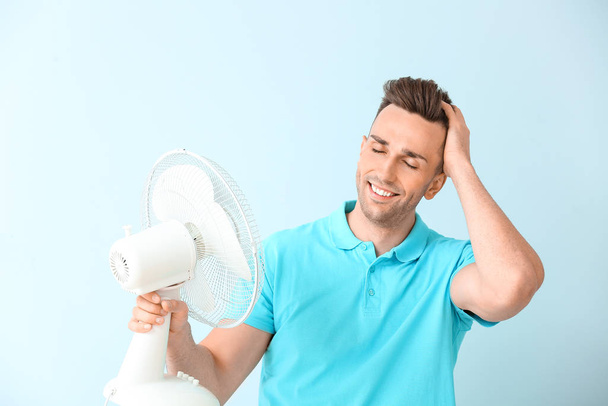 Young man with electric fan on color background - Fotografie, Obrázek