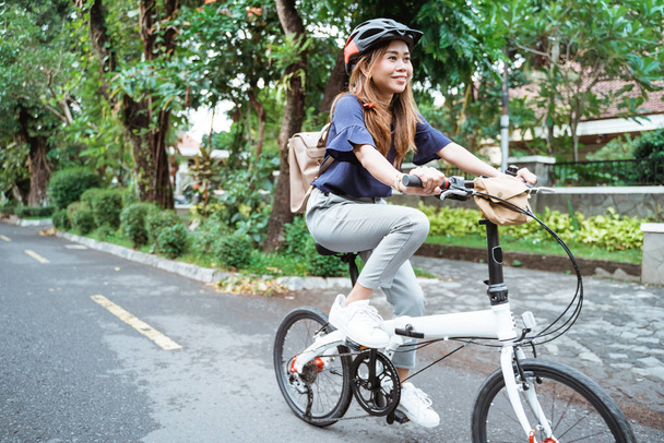 Asian young woman goes wearing a helmet and a bag riding her folding bicycle - Fotó, kép