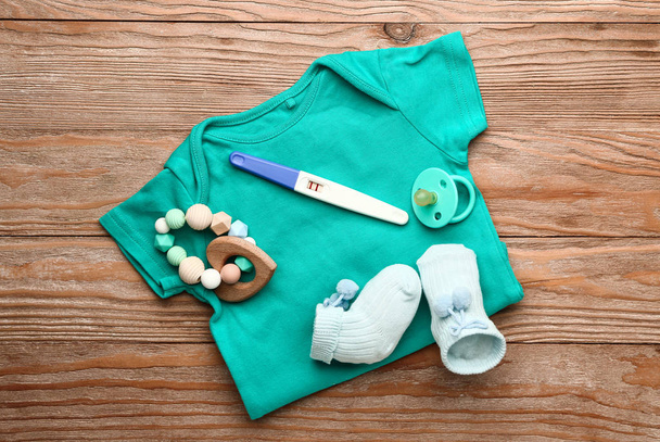 Těhotenský test, dětské oblečení a hračka na dřevěném pozadí - Fotografie, Obrázek
