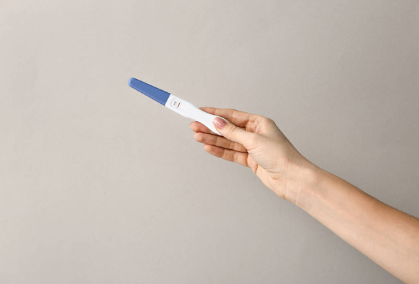 Θηλυκό χέρι με τεστ εγκυμοσύνης σε γκρίζο φόντο - Φωτογραφία, εικόνα