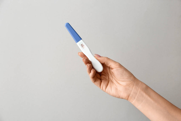 Θηλυκό χέρι με τεστ εγκυμοσύνης σε γκρίζο φόντο - Φωτογραφία, εικόνα