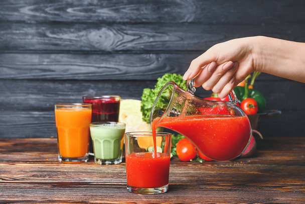 Женщина наливает свежий овощной сок в стакан на стол
 - Фото, изображение