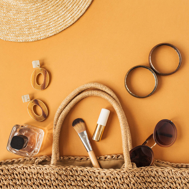 Hasır şapka, içinde kadın aksesuarları (güneş gözlüğü, küpe, parfüm, bilezik, ruj, fırça) bulunan rattan plaj çantası. Flatlay, yukarıdan bak. Modern moda blog kolajı. - Fotoğraf, Görsel