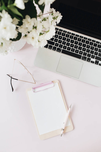 Irodai íróasztal munkaterület laptoppal, virágcsokorral és üres papírral másolás hely mockup írótábla rózsaszín asztalon. Lapos lat, felső nézet szabadúszó kooperatív háttér. - Fotó, kép