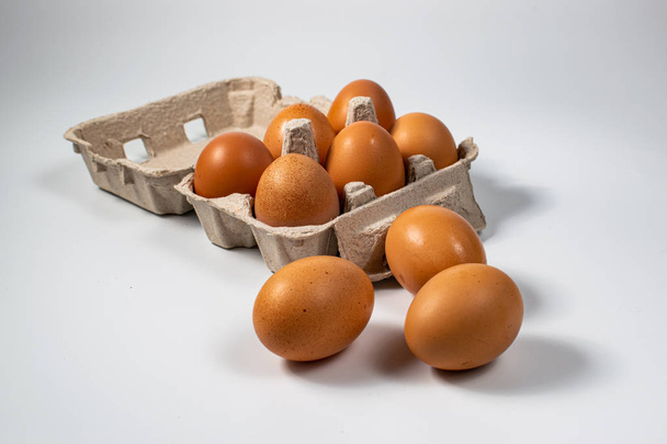 Chicken eggs in a box and on the table, on a white background, waiting to be eaten - Photo, Image