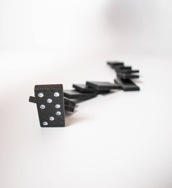 Černé kousky domino s bílými tečkami, uspořádané podle křivky, padající, pouze jeden kus stále stojí - Fotografie, Obrázek