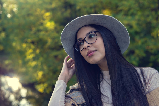 Close up of happy emotionally brunette woman with long hair and hat, smiling at camera. Beautiful model with perfect makeup after salon, posing in park. Concept of fashion and beauty. - Foto, Imagen